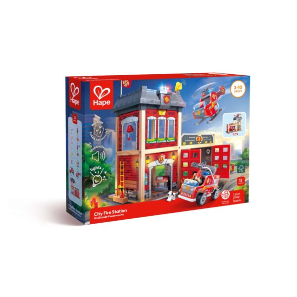 A boxed Hape ‘City Fire Station’ playset for ages 3–10, featuring a multi‑level fire station with a fire truck, helicopter, and small dog figure. The packaging highlights light and sound features, includes 13 pieces