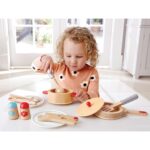 young child playing with wooden cooking pot and pan set with accessories like utensils, salt & pepper shaker and plates.