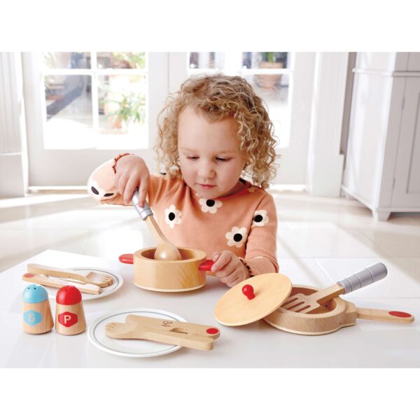 young child playing with wooden cooking pot and pan set with accessories like utensils, salt & pepper shaker and plates.